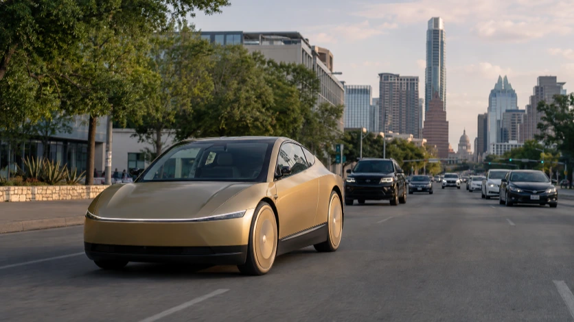 A compact gold driverless taxi without visible steering controls traveling on a city street.